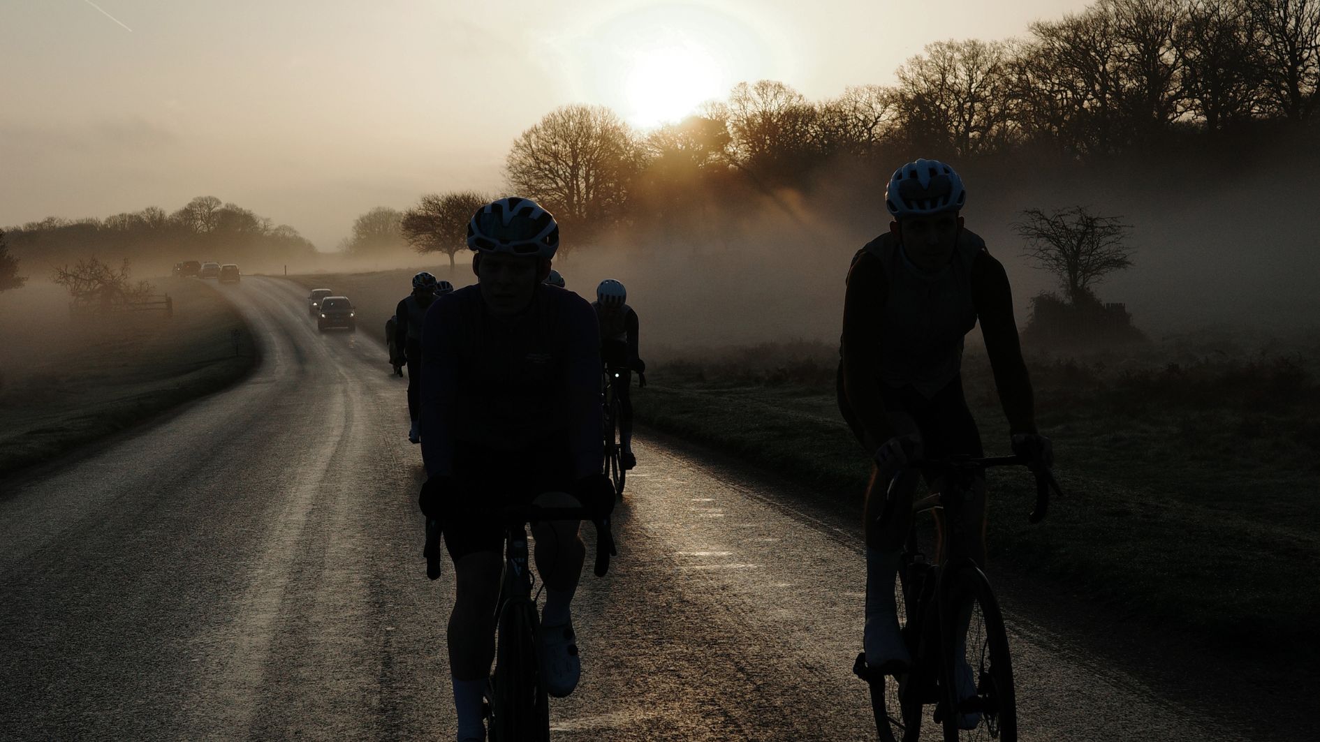 Riders silhouetted on a misty park road at sunrise